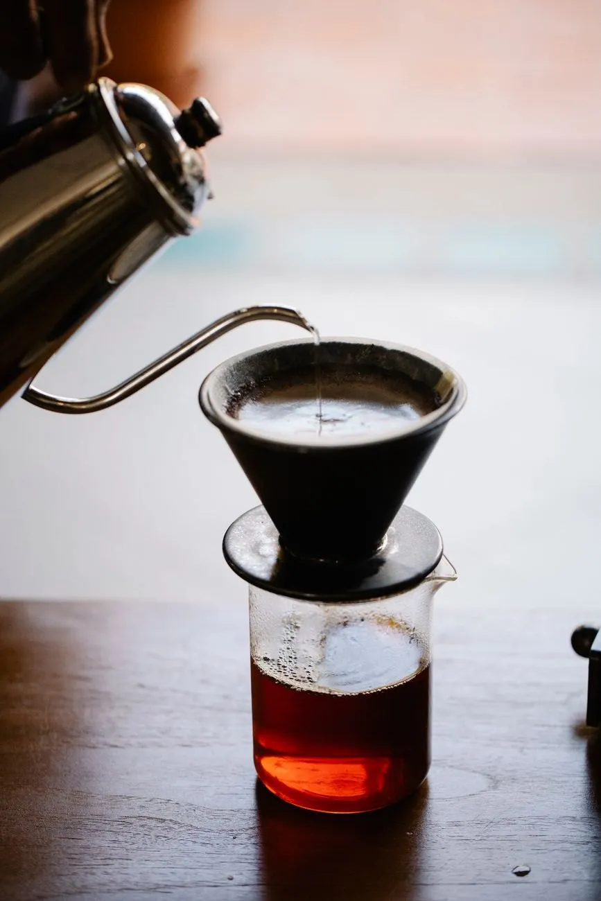 Water poured from a gooseneck kettle into a black pour-over cone over a glass server