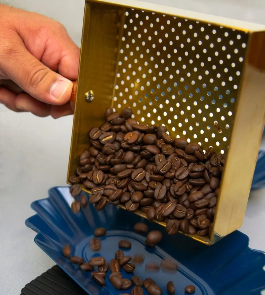 Roasted beans tipped from a brass scoop onto the scale for weighing