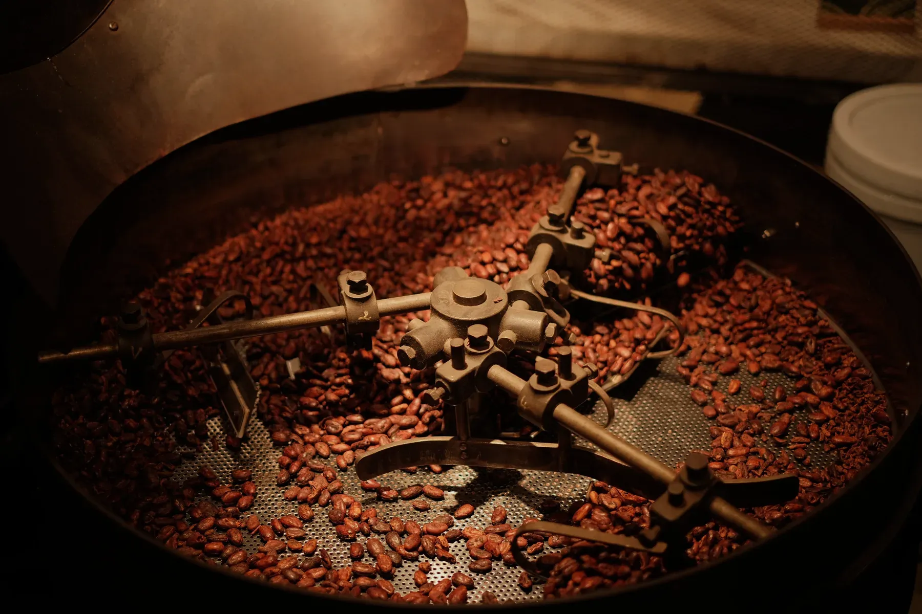 Coffee beans turning in the drum of an industrial roaster, lit from inside the barrel